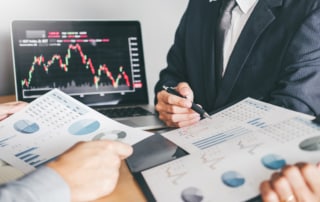 Two people reviewing financial graphs on paper and computer